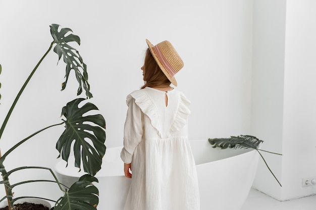 uma garota de vestido branco e chapéu de palha está de costas em uma sala