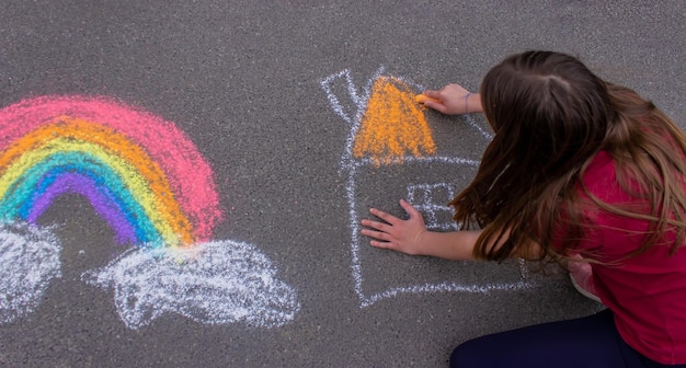 Uma garota desenha um arco-íris uma casa com giz na calçada