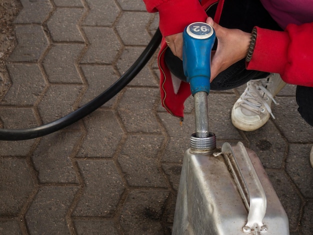 Uma garota despeja gasolina em uma vasilha de metal de uma pistola em um posto de gasolina