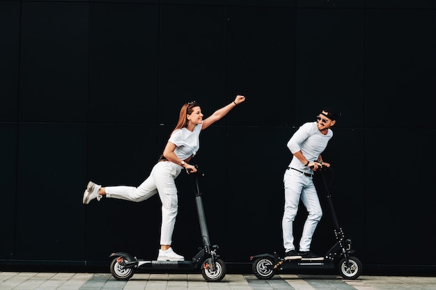 Uma garota e um cara estão andando em scooters elétricos pela cidade, um casal apaixonado em scooters.