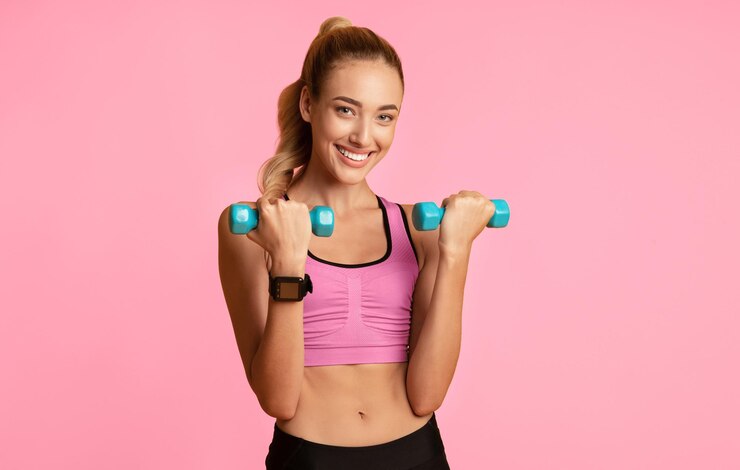 Foto uma garota em forma alegre fazendo exercícios de bíceps com halteres em fundo amarelo em um espaço vazio do estúdio