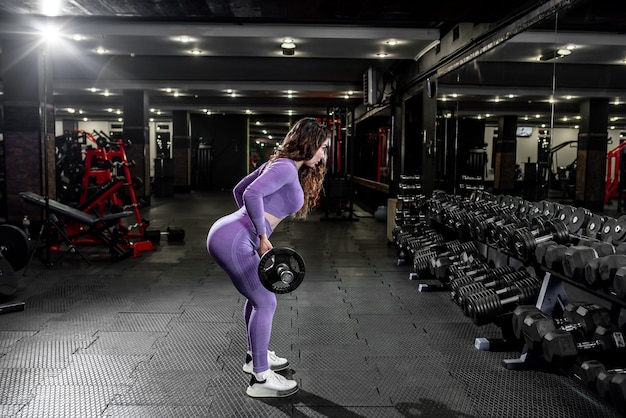 Uma garota em roupas esportivas em uma academia profissional malha com equipamentos de fitness.