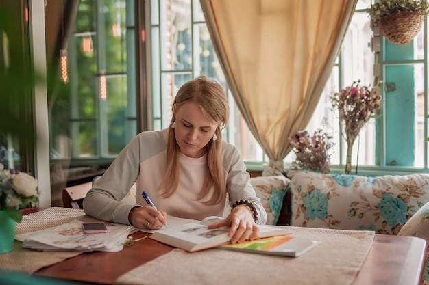 Foto uma garota em um café se senta à mesa e faz anotações em um caderno.