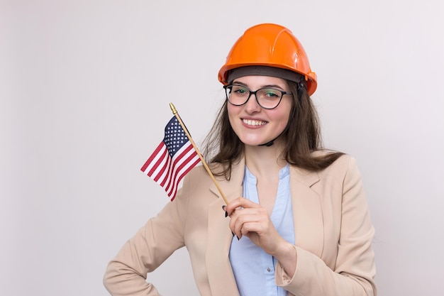 Uma garota em um capacete de construção e uma bandeira americana fica feliz em um fundo branco.