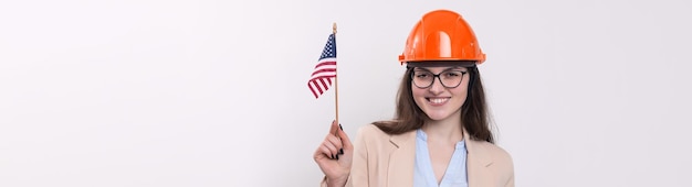 Uma garota em um capacete de construção e uma bandeira americana fica feliz em um fundo branco