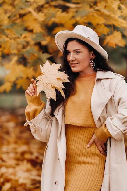 Uma garota em um casaco branco e um chapéu sorri em um outono Park.Retrato de uma mulher no outono dourado.
