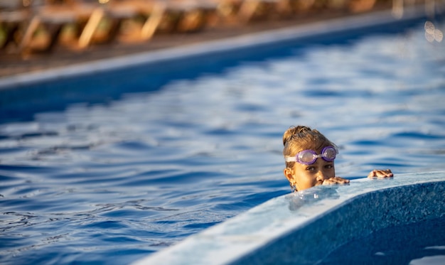 Uma garota em um maiô brilhante com óculos de natação mergulha em uma piscina com água transparente