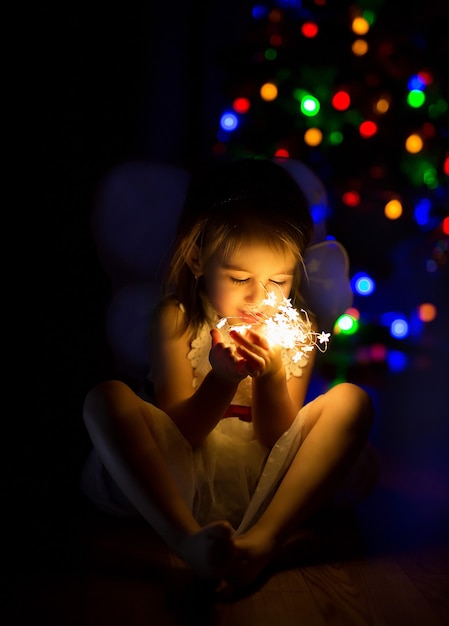 Uma garota em um quarto escuro com luzes de Natal brilhantes nas mãos