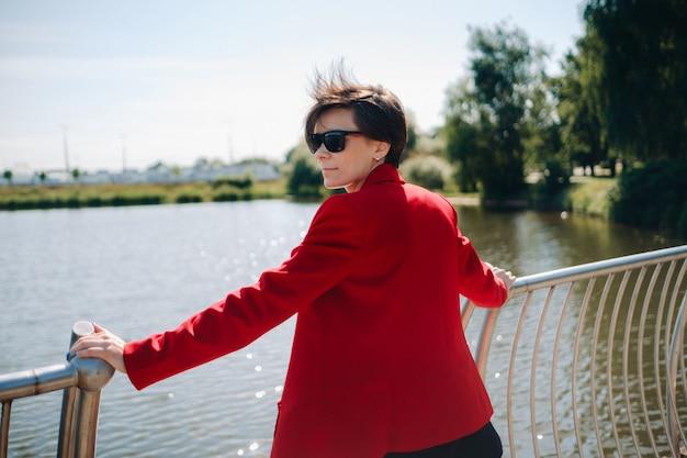 Uma garota em um terno vermelho está em um píer perto do lago