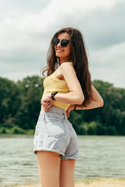 Uma garota em um top amarelo e shorts fica em uma praia