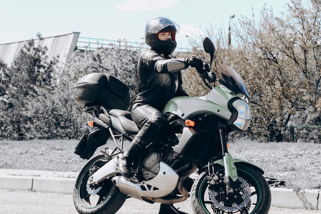 Uma garota em um traje de proteção e um capacete preto se senta em uma motocicleta esportiva