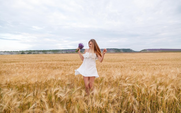 Uma garota em um vestido branco e com um buquê de lavanda em um campo de trigo