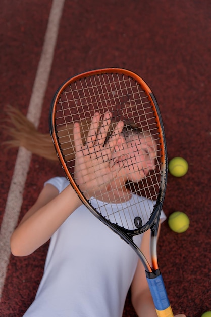 Uma garota em um vestido branco esportivo fica em uma quadra de tênis e segura um retrato de raquete de uma garota na quadra de tênis