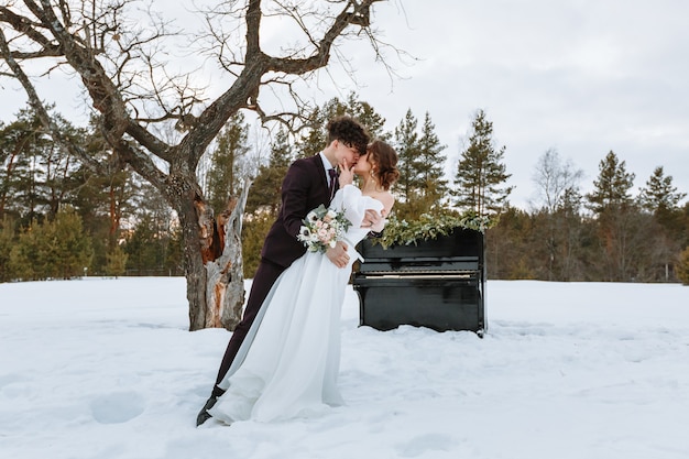 Uma garota em um vestido de noiva e um jovem estão de pé ao lado do piano.