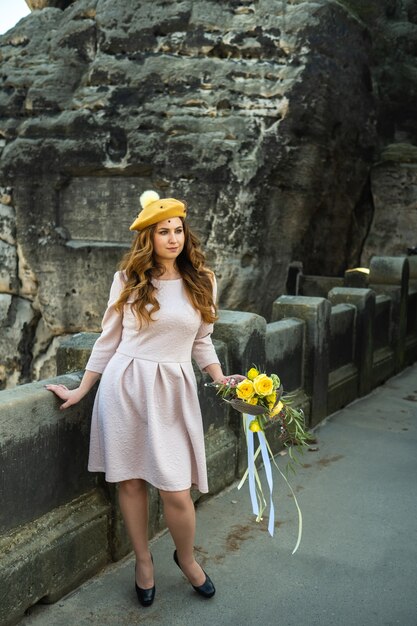 Foto uma garota em um vestido rosa e um chapéu com um buquê de flores na superfície das montanhas e desfiladeiros na saxônia suíça, alemanha, bastei.