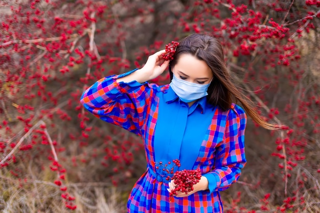 Uma garota em um vestido xadrez e uma máscara no contexto de um arbusto com frutas vermelhas