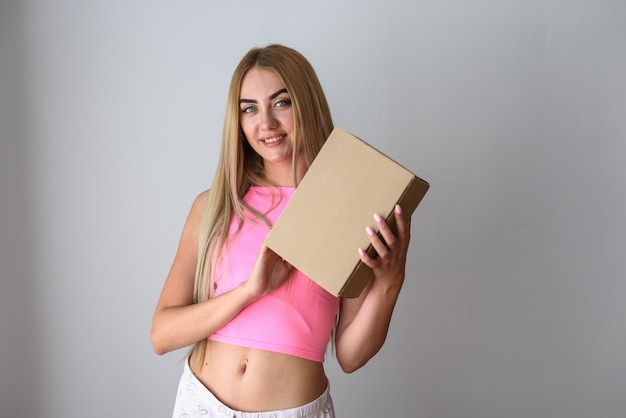 Uma garota em uma camiseta rosa em um fundo cinza segura uma caixa limpa sem logotipos nas mãos