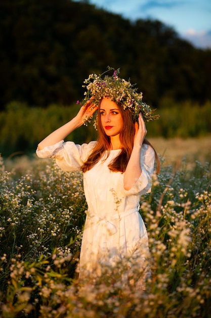 Uma garota em uma coroa de margaridas ao pôr do sol