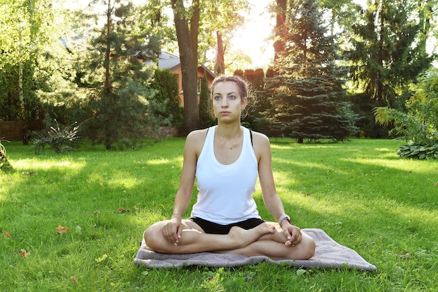 Uma garota em uma pose de osana fazendo ioga no jardim ao nascer do sol