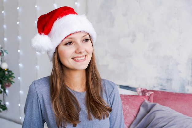 Uma garota emocional com chapéu de papai noel e pijama azul senta-se de manhã na cama