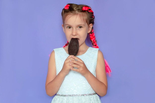 Uma garota encantadora com cabelo rosa lambe sorvete de chocolate em um fundo roxo Sorrindo e rindo Um conceito de verão brilhante