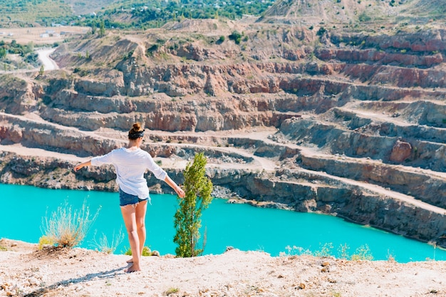 Foto uma garota esguia em uma camisa branca caminha sozinha pela carreira arenosa. no contexto das montanhas e de um lago azul-celeste. paisagem de verão da geórgia