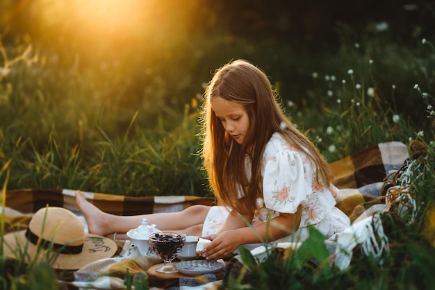 Uma garota está colocando um pedaço de bolo em si mesma durante um piquenique no jardim ao pôr do sol