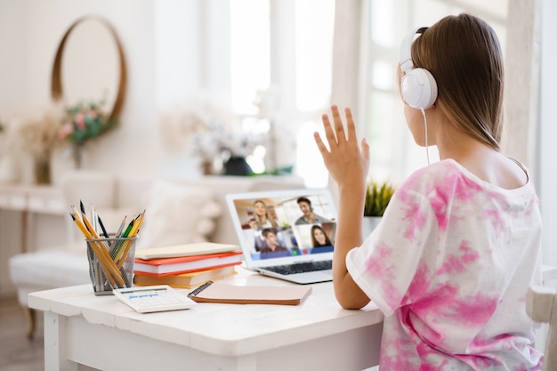 Uma garota está se comunicando por videochamada com colegas de classe no laptop em casa