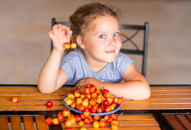 Foto uma garota está sentada em uma mesa de madeira com uma cereja doce nas mãos