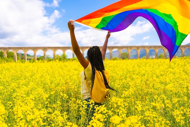 Uma garota étnica negra com tranças segurando a bandeira LGBT em um campo de flores amarelas conceito de mulheres livres de lésbicas do dia do orgulho