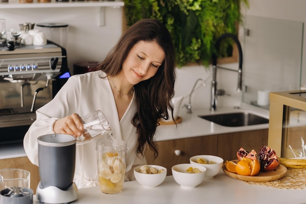 Uma garota faz um coquetel de desintoxicação de frutas na cozinha Dieta para perda de peso