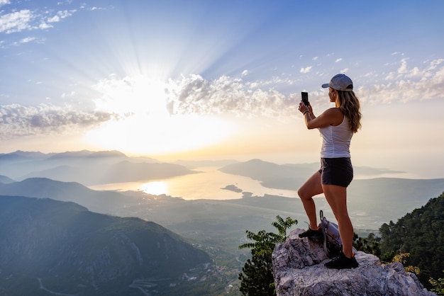 Uma garota feliz com uma mochila fotografa as paisagens marítimas de montenegro do topo da montanha