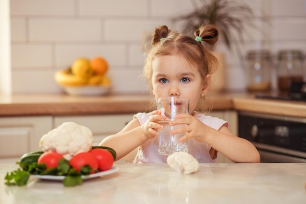 Uma garota feliz de 23 anos na cozinha em casa ou no jardim de infância come vegetais deliciosos e saudáveis para o almoço