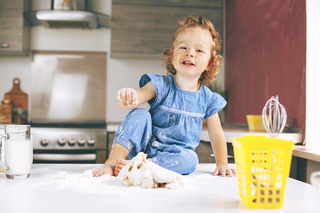 Uma garota feliz está sentada na mesa e amassando a massa