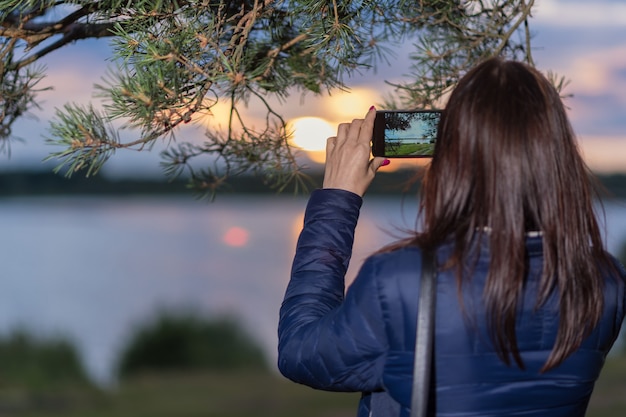 Uma garota fotografa o pôr do sol no lago ao telefone