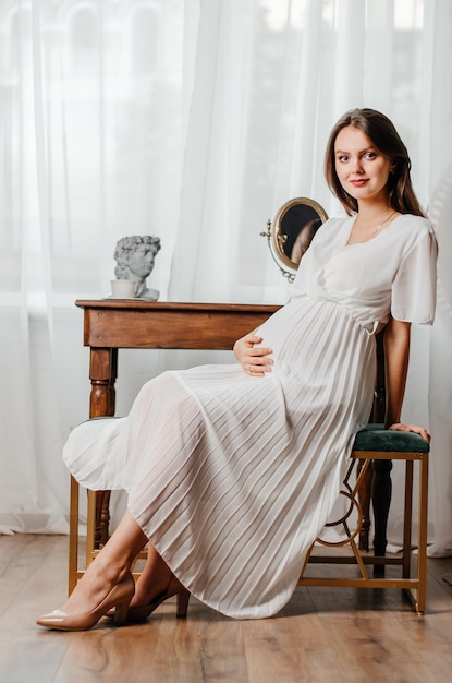 uma garota grávida em um vestido branco senta-se à mesa