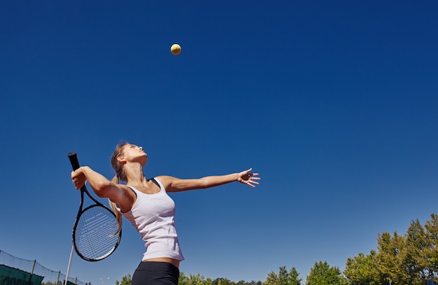 Uma garota jogando tênis na quadra em um lindo dia de sol