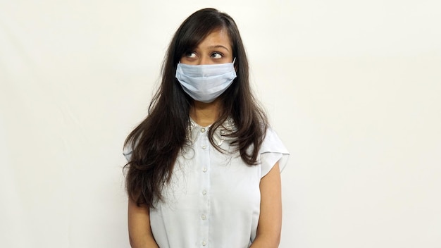 Uma garota jovem da Ásia usando uma máscara facial médica e olhando para um espaço em branco superior