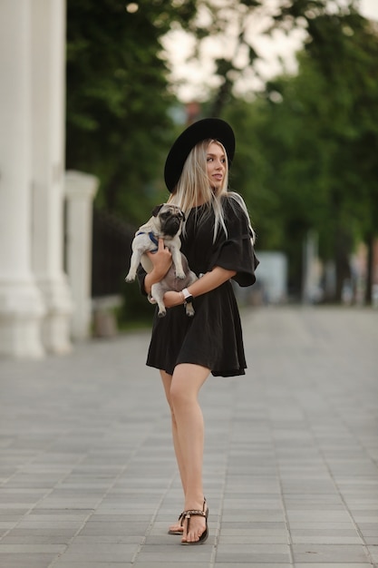 Uma garota jovem e bela modelo no verão curto vestido alegremente andando em uma rua da cidade com seu pequeno cachorro fofo.