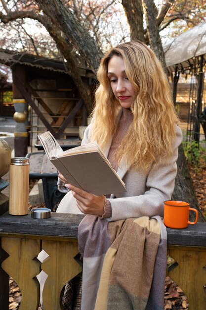 Uma garota lê um livro no terraço no outono e bebe chá