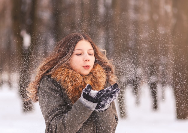 Uma garota leitosa soprando na neve com as mãos na natureza no inverno em um dia ensolarado