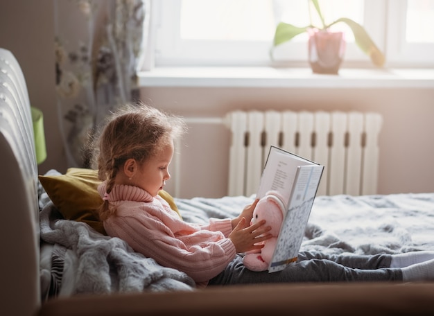 Uma garota lendo um livro em um quarto deitada em uma cama