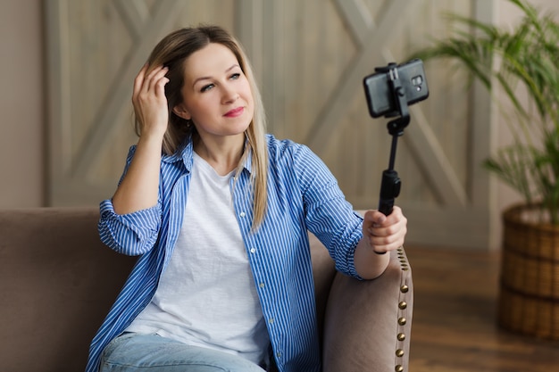 Uma garota loira com uma camisa olha para a tela do telefone para tirar uma selfie