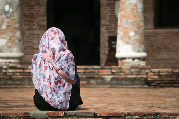 Uma garota muçulmana usa hijab e sentado em frente a arquitetura antiga.