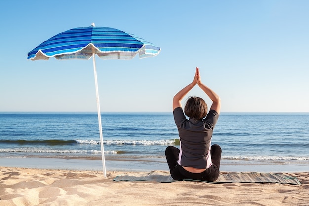 Uma garota na praia pratica aulas de ioga. Verão na areia.