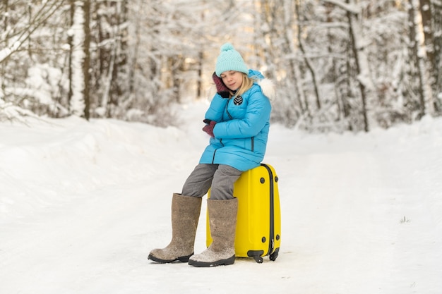 Uma garota no inverno com botas de feltro sentada em uma mala em um dia gelado de neve