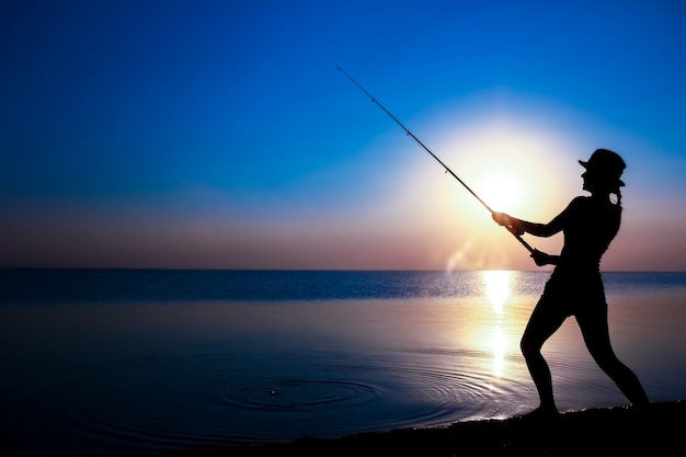 Uma garota pescadora feliz pega peixes à beira-mar em uma viagem de silhueta