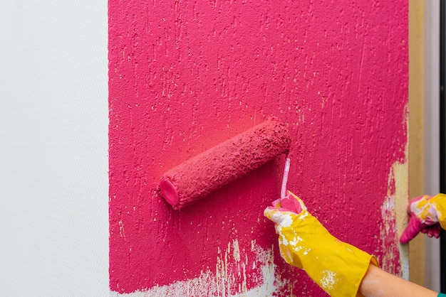 Uma garota pinta um close de parede com um rolo em rosa em seu novo apartamento Renovação do interior e um novo apartamento Housewarming e uma hipoteca desejável