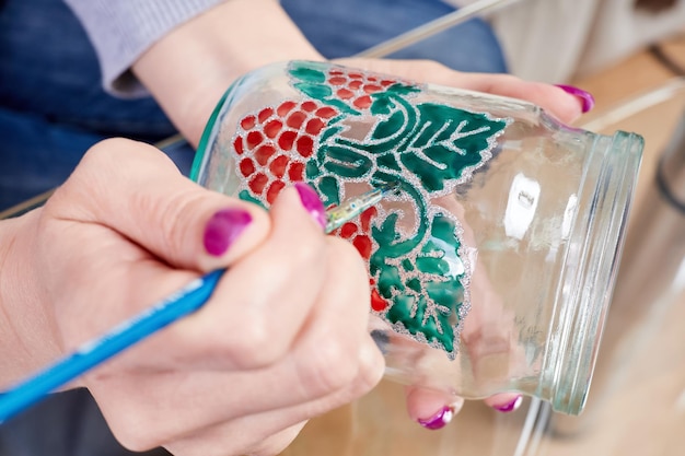 Uma garota pinta uma jarra de vidro com tintas de vitrais