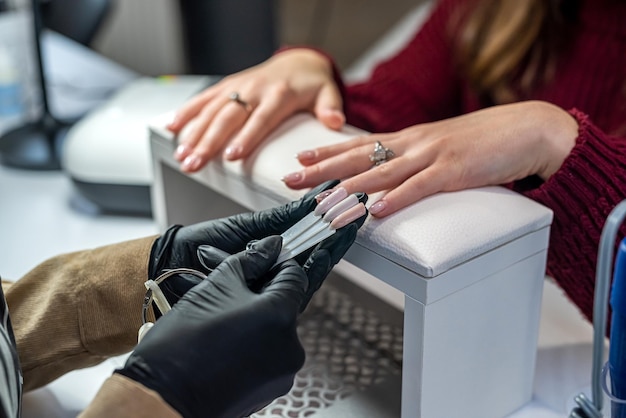Uma garota que é manicure trabalha nas unhas de sua cliente que foi fazer as unhas durante uma pandemia. O conceito de salão de beleza. Conceito de manicure